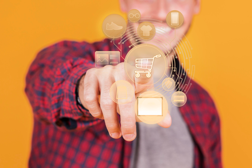 A smiling person in a red plaid shirt pointing toward a virtual shopping cart icon surrounded by digital product icons