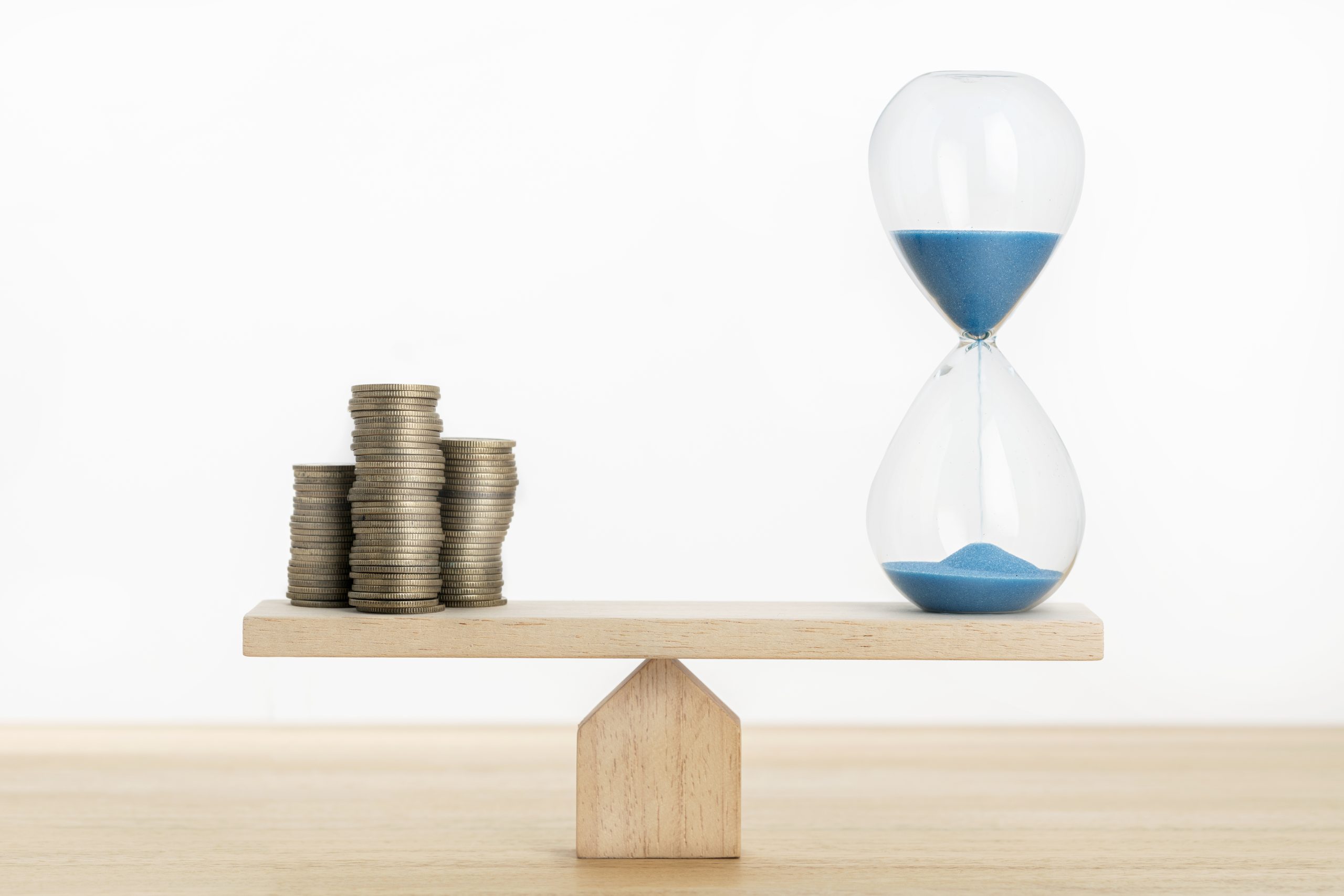  A wooden balance scale with stacks of coins on one side and an hourglass with blue sand on the other