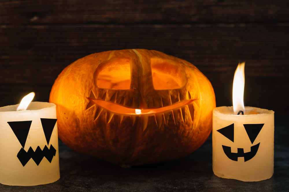 Carved pumpkin with a glowing smile and two lit Halloween-themed candles