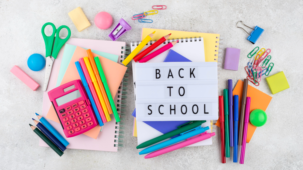 Assorted back-to-school supplies including notebooks, pens, pencils, scissors, a calculator, and colorful stationery arranged on a desk