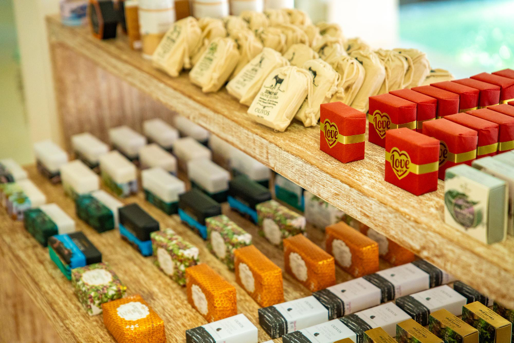 A neatly arranged wooden shelf displaying rows of handcrafted soap bars in various colors, shapes, and packaging styles